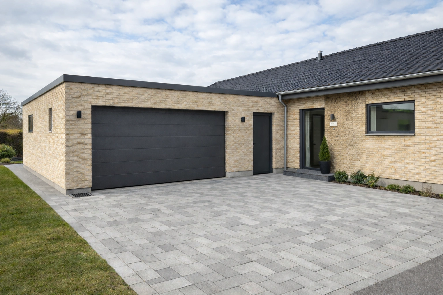 Moderniseret dansk 70’er parcelhus med integreret garagetilbygning i lyse mursten, mørk træbeklædning og antracit garageport ved grå fliseindkørsel.